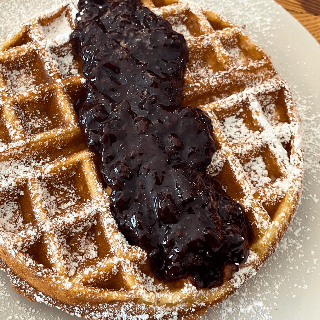 Belgium Waffle with powdered sugar and blueberry compote on top.