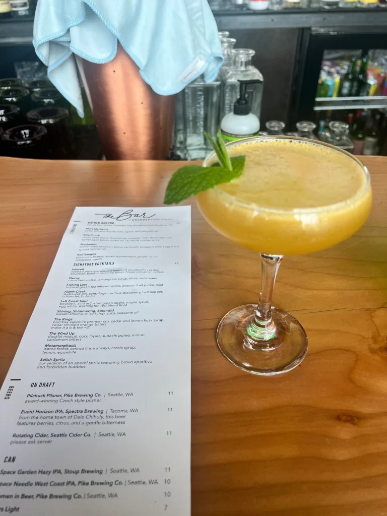 Yellow cocktail next to white drink menu