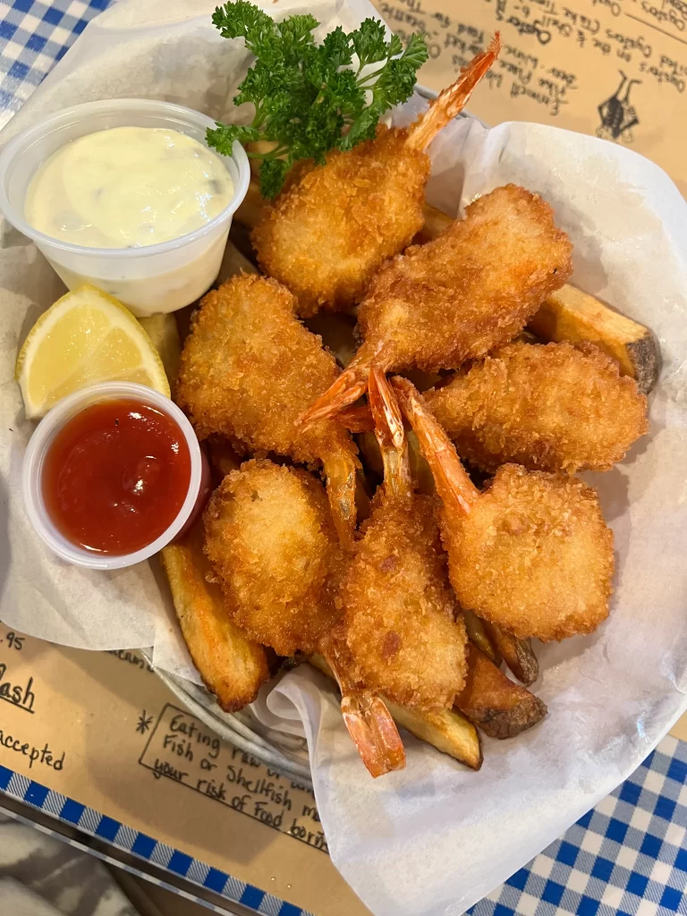 A basket of fried shrimps and chips with tartar sauce and ketchup
